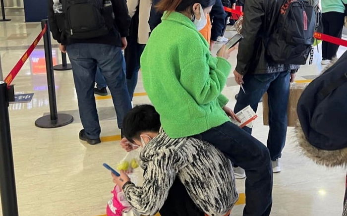 해외여행 공항 검색대 대기 중 여친 위해 ‘인간 의자’ 돼준 남친...“로맨틱 vs 남자가 노예냐”