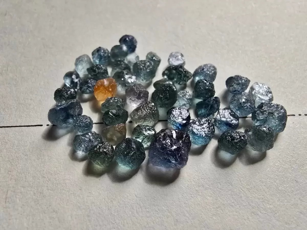 Pile of raw, uncut sapphires in various shades of blue, green, purple, and orange.