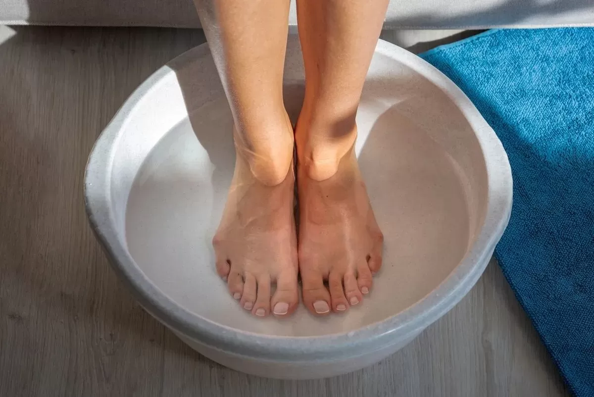 Woman soaks her feet in tub of water in home