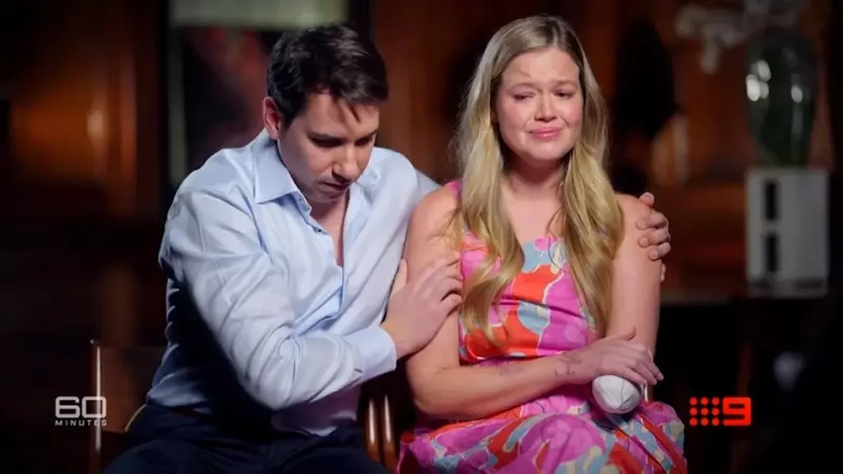 A man comforts a crying woman with blonde hair who is wearing a colorful dress.